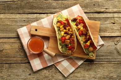 Photo of Tasty vegetarian tacos served with sauce on wooden table, flat lay