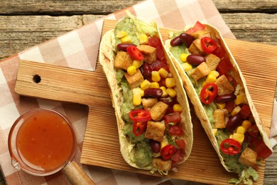 Photo of Tasty vegetarian tacos served with sauce on wooden table, flat lay