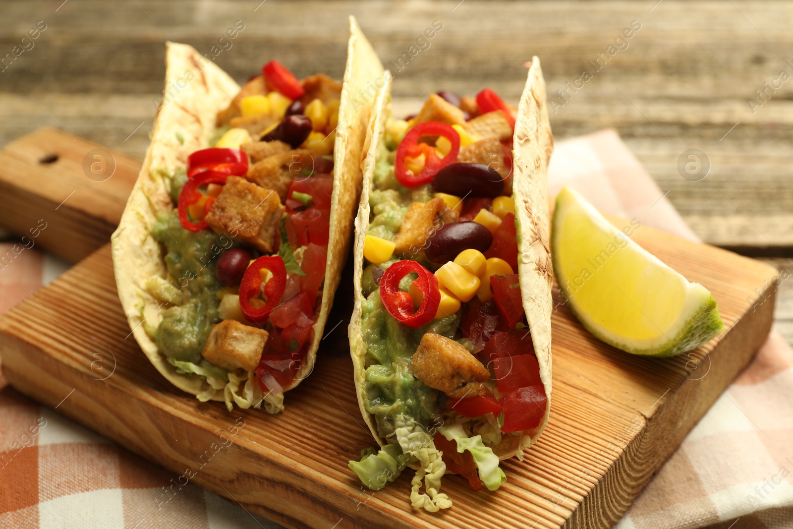 Photo of Tasty vegetarian tacos with beans, tofu, vegetables, guacamole and lime on wooden table, closeup