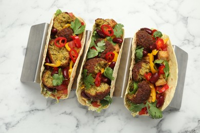 Photo of Tasty vegetarian tacos with falafel, tofu, beans and vegetables on white marble table, top view
