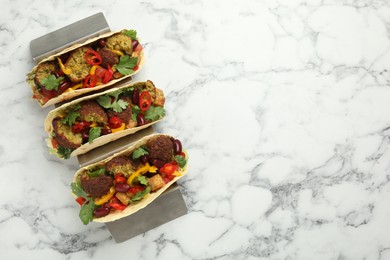 Photo of Tasty vegetarian tacos with falafel, tofu, beans and vegetables on white marble table, top view. Space for text