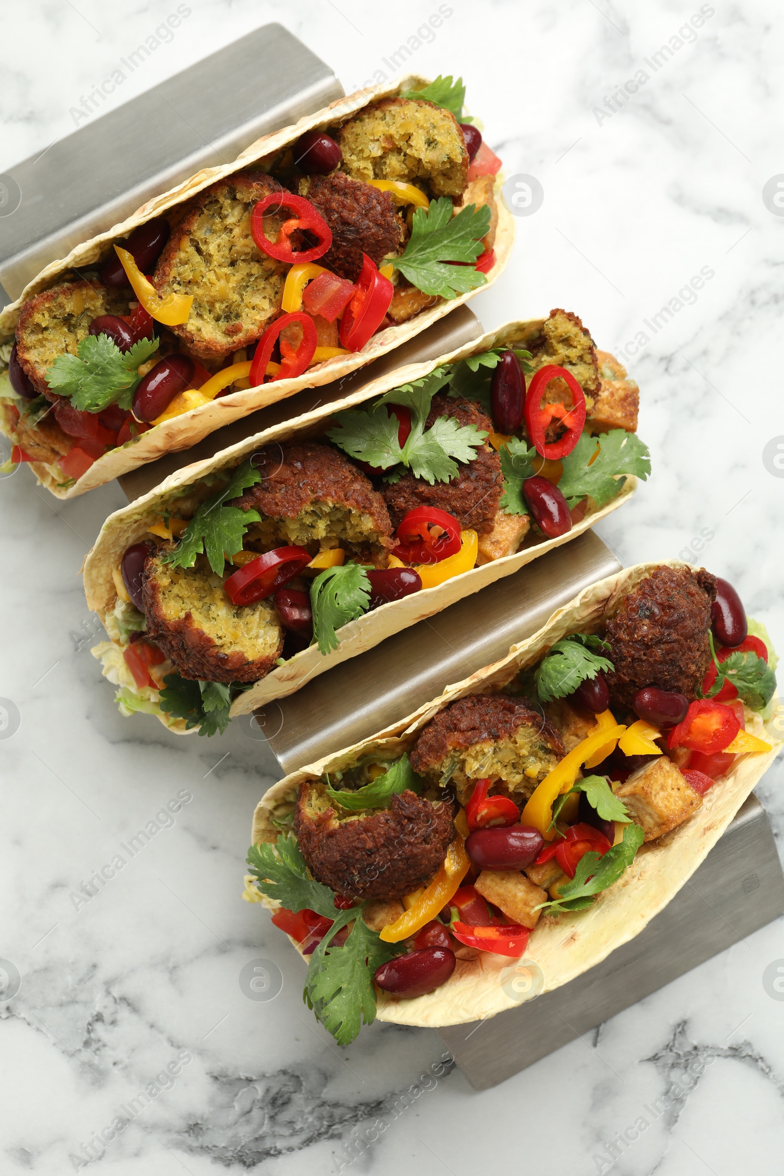 Photo of Tasty vegetarian tacos with falafel, tofu, beans and vegetables on white marble table, top view