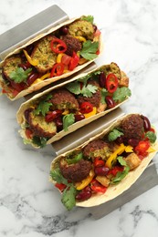 Photo of Tasty vegetarian tacos with falafel, tofu, beans and vegetables on white marble table, top view