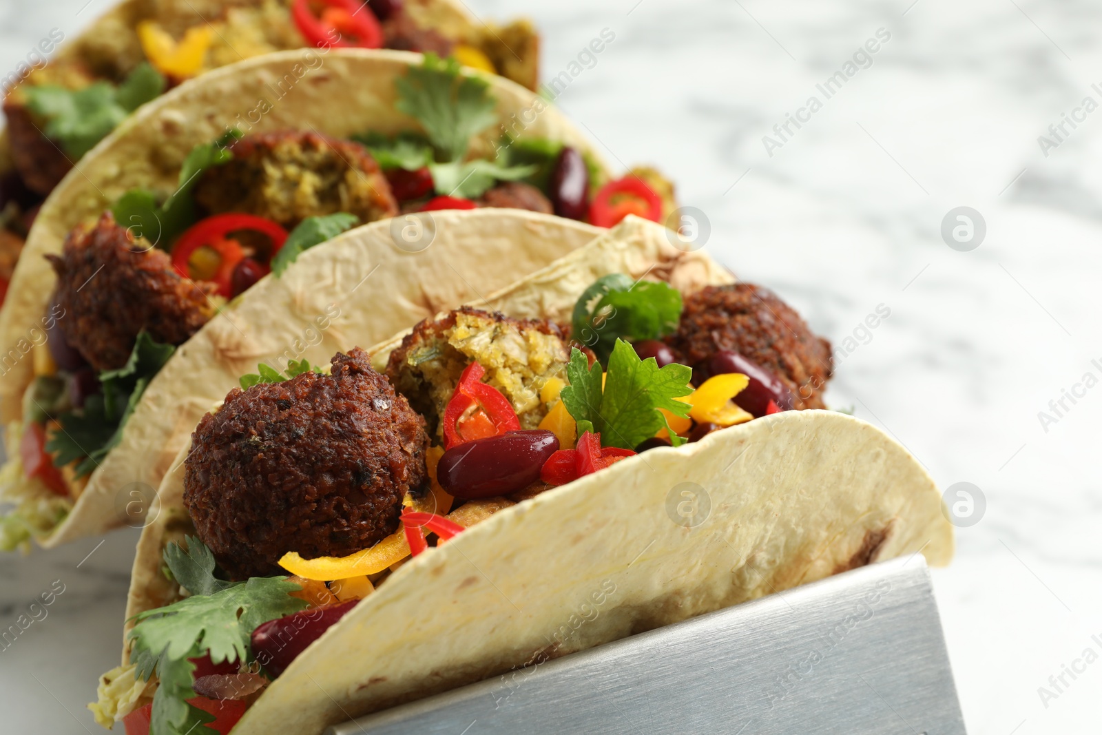 Photo of Tasty vegetarian tacos with falafel, tofu, beans and vegetables on white marble table, closeup