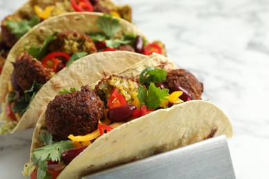 Photo of Tasty vegetarian tacos with falafel, tofu, beans and vegetables on white marble table, closeup