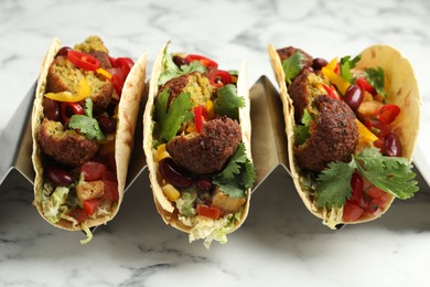Photo of Tasty vegetarian tacos with falafel, tofu, beans and vegetables on white marble table, closeup