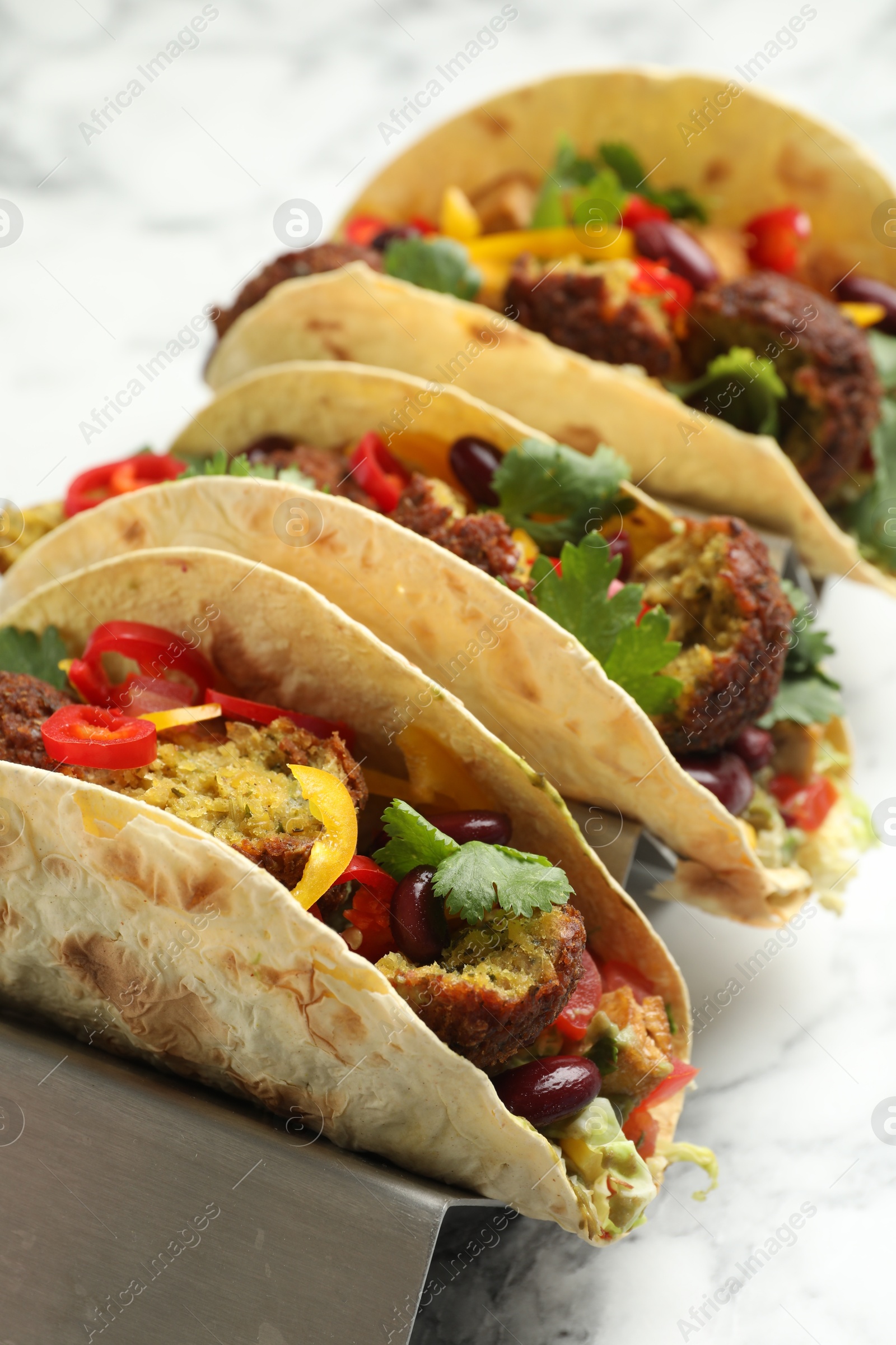 Photo of Tasty vegetarian tacos with falafel, tofu, beans and vegetables on white marble table, closeup