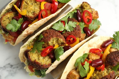 Photo of Tasty vegetarian tacos with falafel, tofu, beans and vegetables on white marble table, above view