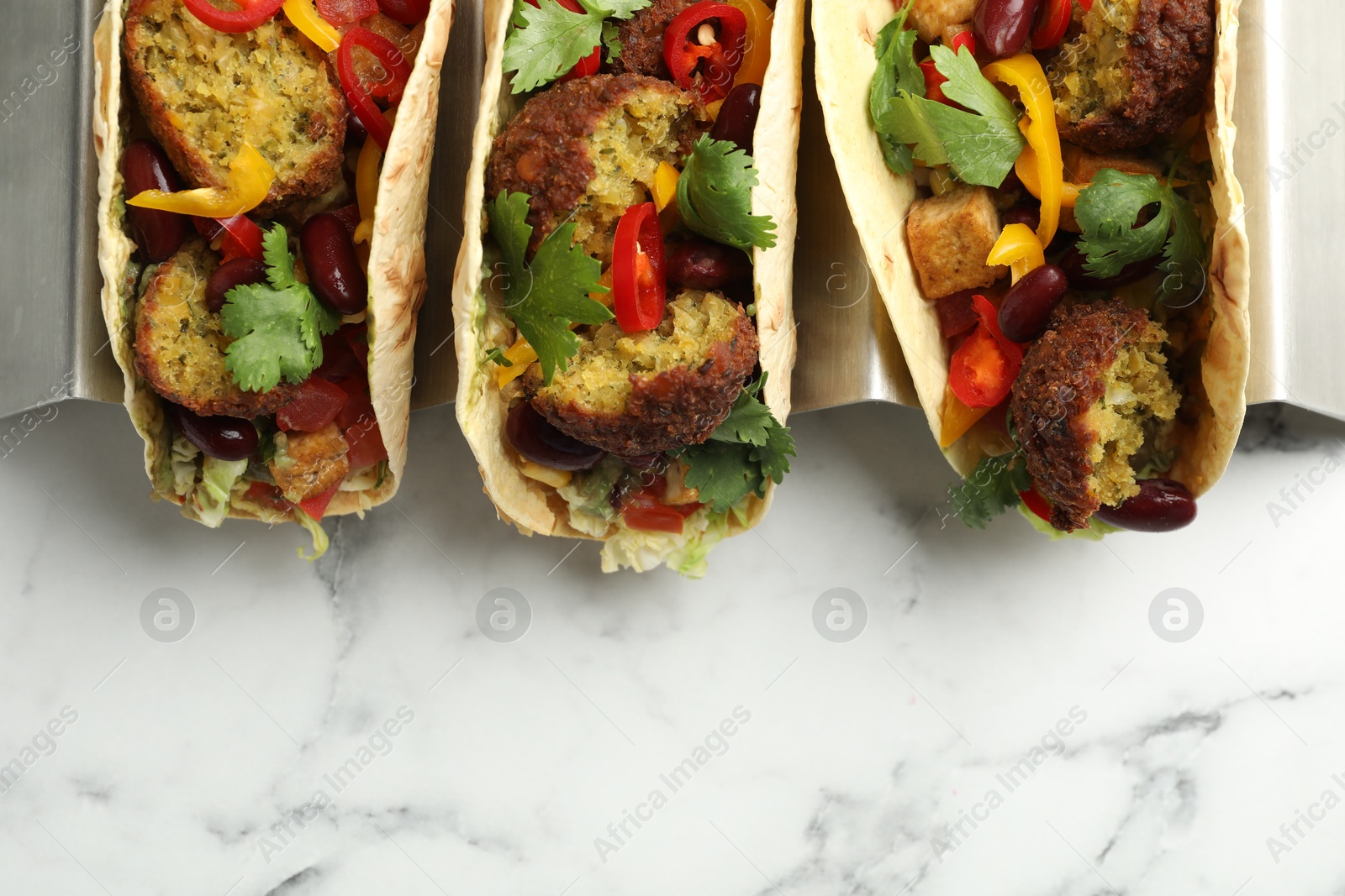 Photo of Tasty vegetarian tacos with falafel, tofu, beans and vegetables on white marble table, top view. Space for text