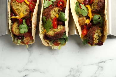 Photo of Tasty vegetarian tacos with falafel, tofu, beans and vegetables on white marble table, top view. Space for text