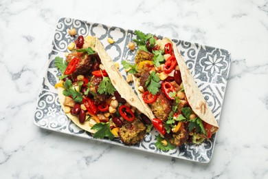 Photo of Tasty vegetarian tacos with falafel, tofu, beans and vegetables on white marble table, top view