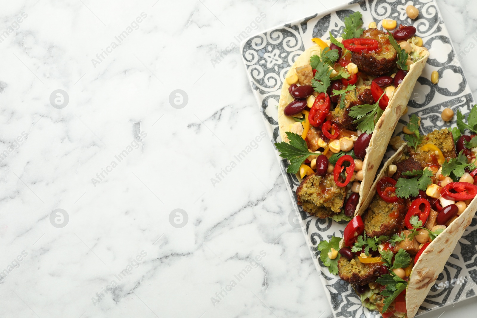 Photo of Tasty vegetarian tacos with falafel, tofu, beans and vegetables on white marble table, top view. Space for text