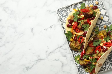 Photo of Tasty vegetarian tacos with falafel, tofu, beans and vegetables on white marble table, top view. Space for text