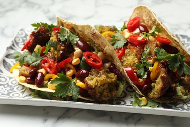 Photo of Tasty vegetarian tacos with falafel, tofu, beans and vegetables on white marble table, closeup