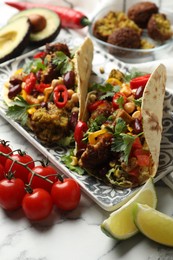 Photo of Tasty vegetarian tacos with falafel and other ingredients on white marble table, closeup