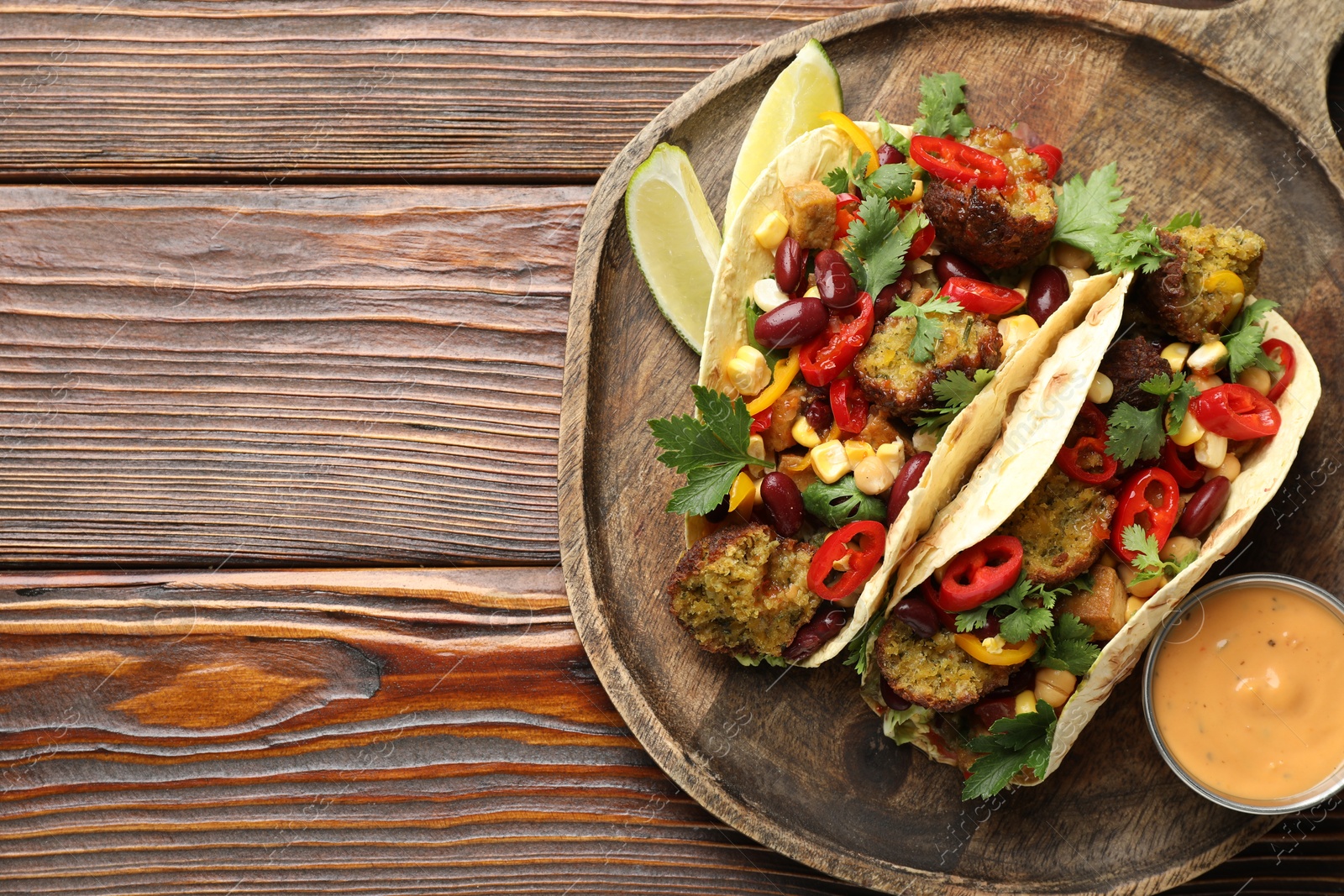 Photo of Tasty vegetarian tacos with falafel served with sauce on wooden table, top view. Space for text