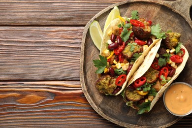 Photo of Tasty vegetarian tacos with falafel served with sauce on wooden table, top view. Space for text
