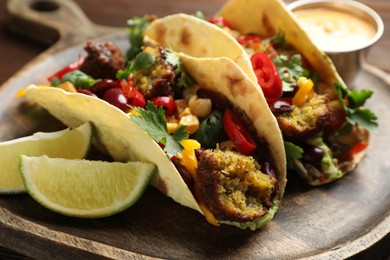 Photo of Tasty vegetarian tacos with falafel served with sauce on table, closeup