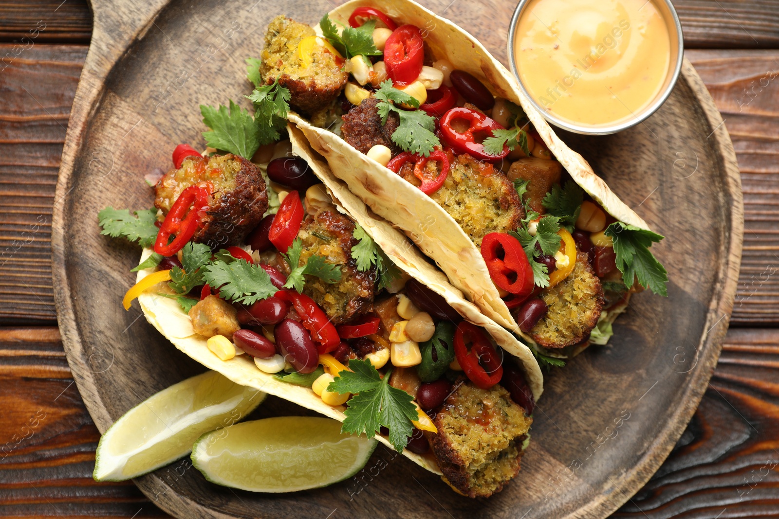 Photo of Tasty vegetarian tacos with falafel served with sauce on wooden table, top view