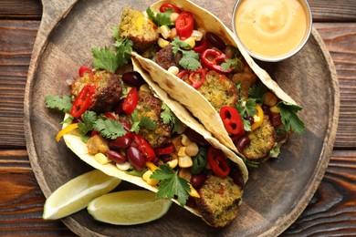 Photo of Tasty vegetarian tacos with falafel served with sauce on wooden table, top view