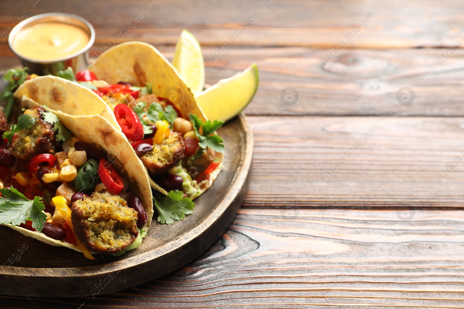 Photo of Tasty vegetarian tacos with falafel served with sauce on wooden table, closeup. Space for text