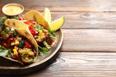 Photo of Tasty vegetarian tacos with falafel served with sauce on wooden table, closeup. Space for text