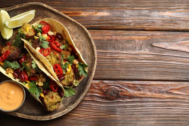 Photo of Tasty vegetarian tacos with falafel served with sauce on wooden table, top view. Space for text