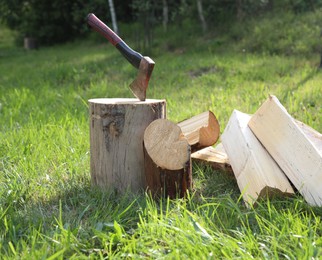 Photo of Metal axe, chopped firewood and wooden log on green grass outdoors