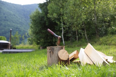 Photo of Metal axe, chopped firewood and wooden log on green grass outdoors. Space for text