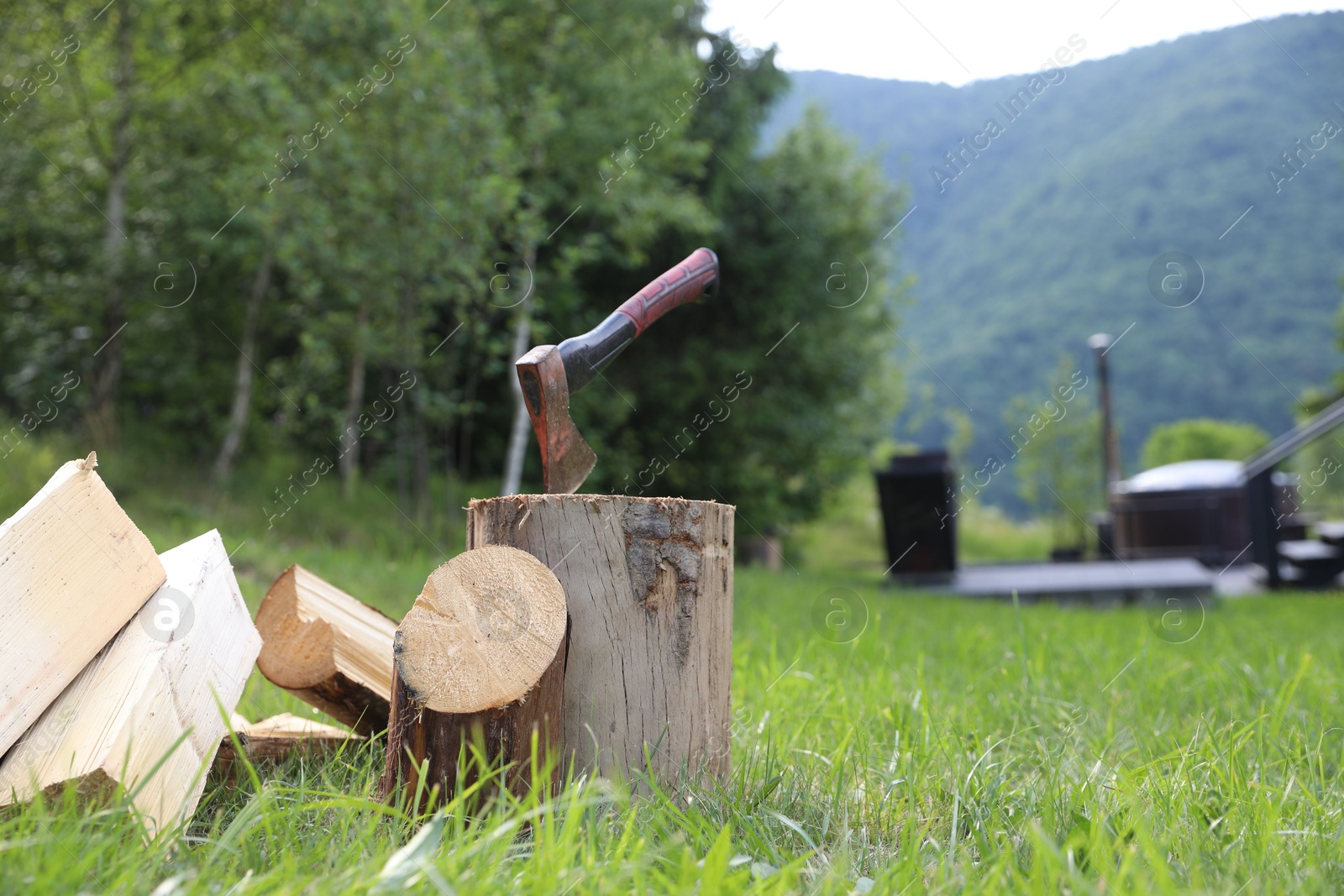 Metal axe, chopped firewood and wooden log on green grass outdoors. Space for text Photo of Metal axe, chopped firewood and wooden log on green grass outdoors. Space for text
