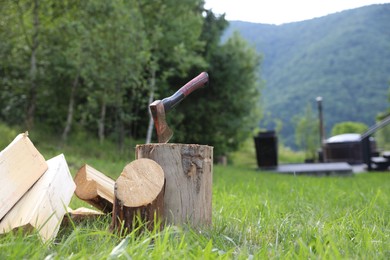 Photo of Metal axe, chopped firewood and wooden log on green grass outdoors. Space for text