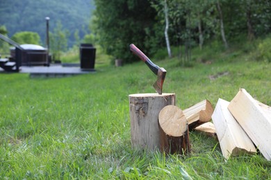 Photo of Metal axe, chopped firewood and wooden log on green grass outdoors. Space for text