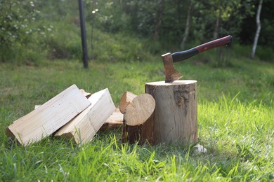 Photo of Metal axe, chopped firewood and wooden log on green grass outdoors