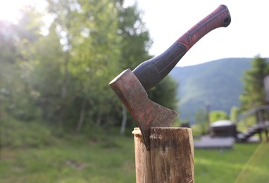 Photo of Metal axe on wooden log outdoors, closeup. Space for text