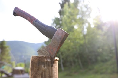 Photo of Metal axe on wooden log outdoors, closeup. Space for text