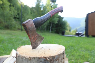 Photo of Metal axe and wooden log outdoors, closeup