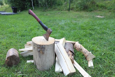 Photo of Metal axe, chopped firewood and wooden log on green grass outdoors