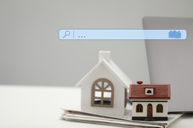 Image of Searching for housing online. Laptop and house models on table. Search bar near computer