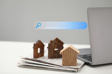 Image of Searching for housing online. Laptop and house models on table. Search bar near computer
