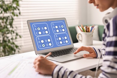 Image of Woman passing online test on laptop and writing in notebook at table, closeup