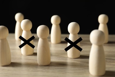 Image of Dismissal. Two human figures with black crosses among others on wooden table