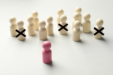 Image of Dismissal. Three human figures with black crosses among others on white table. Pink figure - boss or HR manager