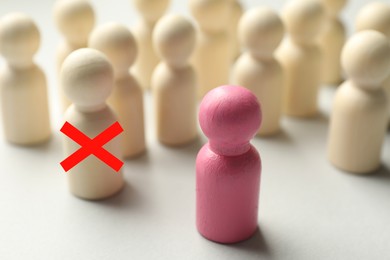 Image of Dismissal. One human figure with red cross among others on white table. Pink figure - boss or HR manager