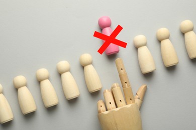 Image of Dismissal. Mannequin hand throwing pink human figure with red cross away on grey background, top view