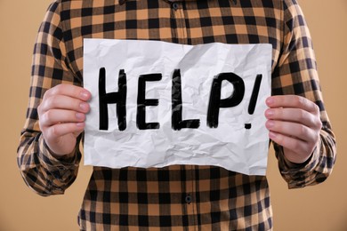 Image of Man holding paper with word Help against pale orange background, closeup