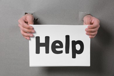 Image of Asking or offering help. Man holding paper with word through holes in grey paper, closeup