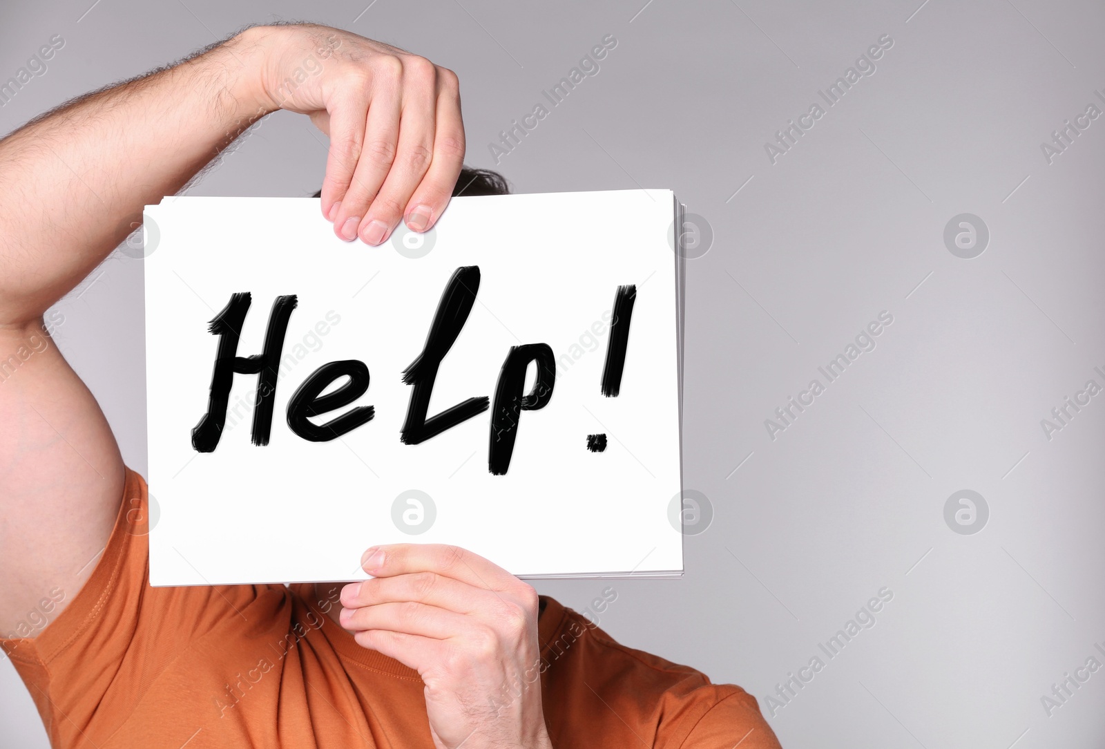 Man holding paper with word Help in front of his face against grey background, closeup Image of Man holding paper with word Help in front of his face against grey background, closeup