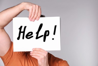 Image of Man holding paper with word Help in front of his face against grey background, closeup
