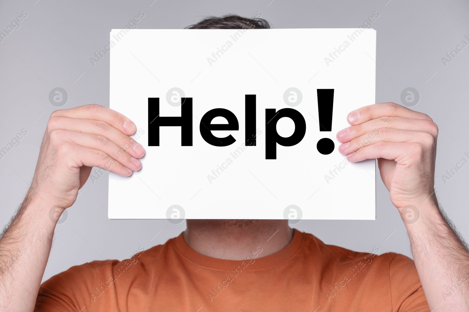 Man holding paper with word Help in front of his face against grey background, closeup Image of Man holding paper with word Help in front of his face against grey background, closeup