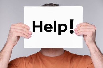 Image of Man holding paper with word Help in front of his face against grey background, closeup